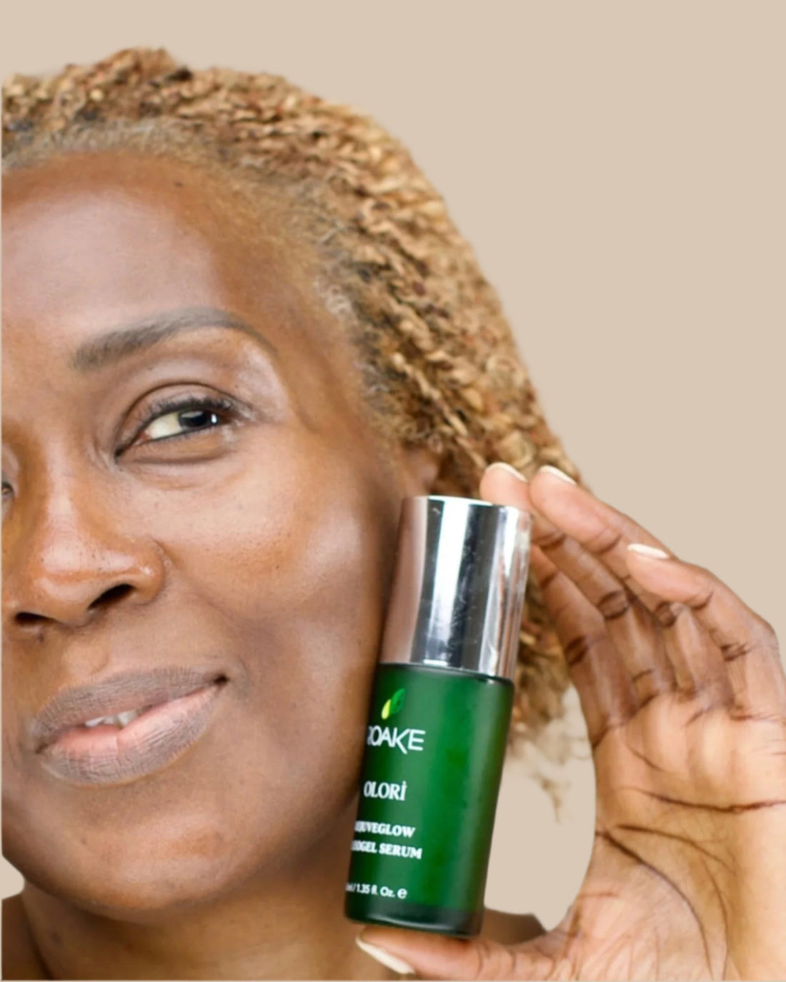 A radiant woman smiling while holding Olorì RejuveGlow Serum to her face.