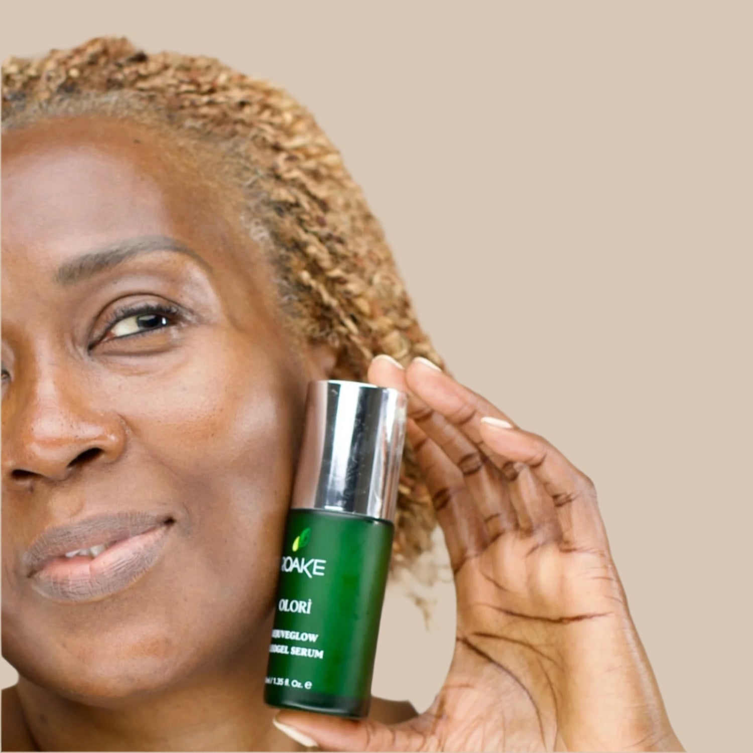 A radiant woman smiling while holding Olorì RejuveGlow Serum to her face.